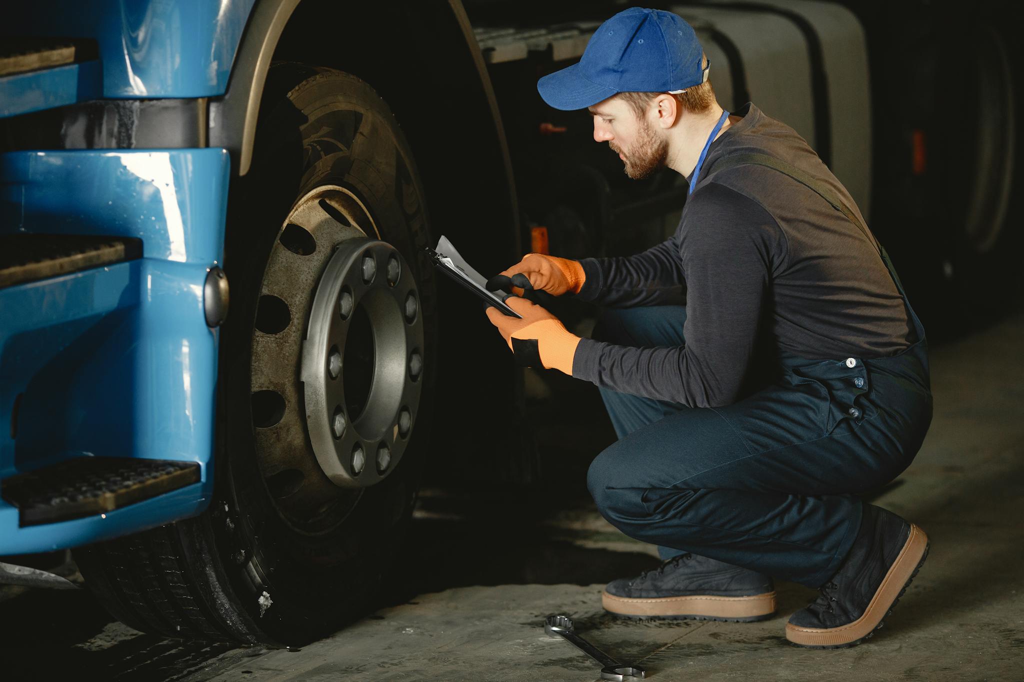 Mechanic checking a truck's wheel using a tablet in an indoor garage setting.